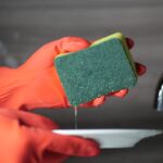 A person with red rubber gloves holding a kitchen sponge